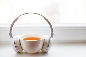 blanco auriculares con un taza de té en el ventana. auriculares en un cuaderno para notas en un blanco antecedentes foto