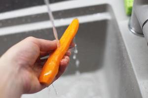 woman washes carrots in the kitchen. raw carrots photo