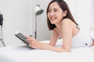 Portrait of white Asian woman with tattoo resting in bed to rest and relax inside white bedroom on her holiday, holiday morning concept. photo