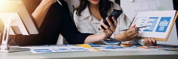 Close up ux developer and ui designer brainstorming about mobile app interface wireframe design on table with customer breif and color code at modern office.Creative digital development agency photo