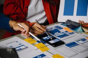 Close up ux developer and ui designer brainstorming about mobile app interface wireframe design on table with customer breif and color code at modern office.Creative digital development agency photo