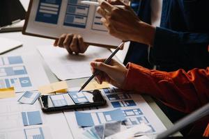 Close up ux developer and ui designer brainstorming about mobile app interface wireframe design on table with customer breif and color code at modern office.Creative digital development agency photo