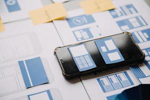 Close up ux developer and ui designer brainstorming about mobile app interface wireframe design on table with customer breif and color code at modern office.Creative digital development agency photo