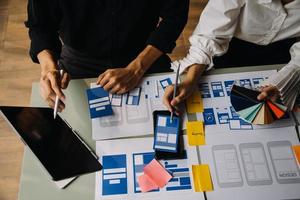 Close up ux developer and ui designer brainstorming about mobile app interface wireframe design on table with customer breif and color code at modern office.Creative digital development agency photo