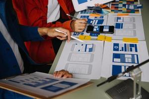 Close up ux developer and ui designer brainstorming about mobile app interface wireframe design on table with customer breif and color code at modern office.Creative digital development agency photo