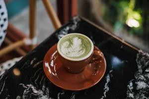 un taza de matcha latté con latté Arte en un negro mármol mesa foto