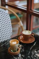 café latté y matcha latté en un negro mármol mesa cerca el ventana foto