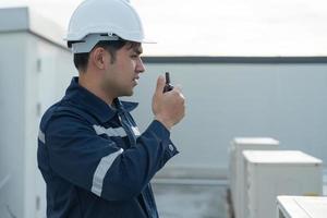 Asian maintenance engineer work on the roof of factory. contractor inspect compressor system and plans installation of air condition systems in construction. technology, walky talky, maintenance photo