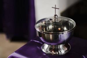 A silver bowl with a cross on it sits on a purple cloth. photo