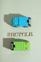 Toy garbage trucks and recycle text on a green background top view, flat lay photo