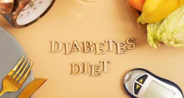 Diabetes diet text with plate and cutlery, glucose meter on beige background flat lay, top view photo