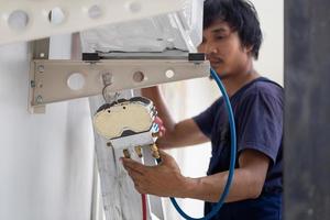 joven reparador fijación aire acondicionador unidad, asiático técnico hombre instalando un aire acondicionamiento en un cliente casa, mantenimiento y reparando conceptos foto