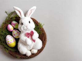 A fluffy toy bunny sits in a nest with easter eggs. photo