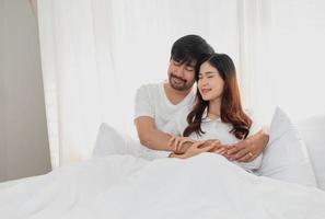 Happy young asian couple embracing, teasing, playing cheerfully in bed at home, romantic time to enhance family bonding. family concept. photo