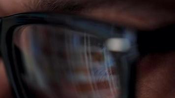 Man in glasses looking on the monitor and surfing Internet. The monitor screen is reflected in the glasses video