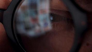 Man in glasses looking on the monitor and surfing Internet. The monitor screen is reflected in the glasses video