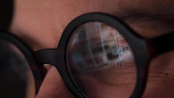 Man in glasses looking on the monitor and surfing Internet. The monitor screen is reflected in the glasses video