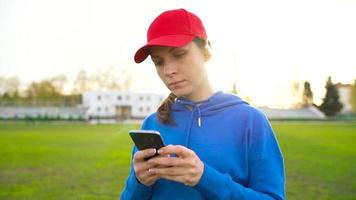 kvinna med trådlös hörlurar och smartphone väljer musik och kör genom de stadion på solnedgång. långsam rörelse video