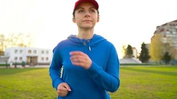 donna con senza fili cuffie e smartphone sceglie musica e corre attraverso il stadio a tramonto. lento movimento video