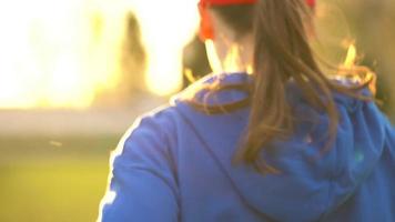 mulher com sem fio fones de ouvido e Smartphone escolhe música e corre através a estádio às pôr do sol. lento movimento video