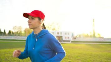 Woman with wireless headphones and smartphone chooses music and runs through the stadium at sunset. Slow motion video