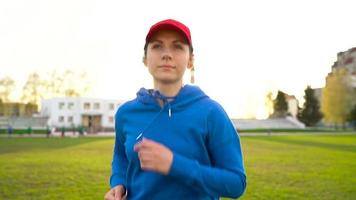 Woman with wireless headphones and smartphone chooses music and runs through the stadium at sunset. Slow motion video