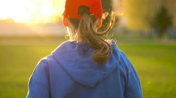 mulher com sem fio fones de ouvido e Smartphone escolhe música e corre através a estádio às pôr do sol. lento movimento video