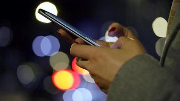 femmina mani utilizzando smartphone su sfocato città luci sfondo video