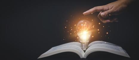 Thinking and creative concept, Hand touch Light bulb on the Book and light bulb style bokeh vintage dark background,Concept The idea of reading books, knowledge, and searching for new ideas. photo