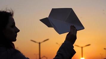 vrouw lanceert papier vliegtuig tegen zonsondergang achtergrond. concept van willen naar Gaan Aan vakantie of reizen video