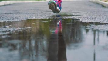 stänga upp skott av ben av en löpare i sneakers. kvinna sporter man joggning utomhus i en parkera, stepping in i grumlig pöl video