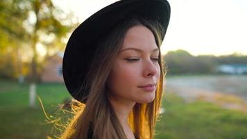 mooi glimlachen meisje in een zwart hoed met een zonsondergang in de achtergrond wandelen buitenshuis video