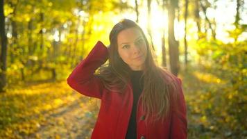 Portrait of a beautiful pensive girl in a red coat with a yellow maple leaf in the background in the autumn forest. Slow motion video