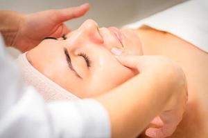 Beautician making lymphatic drainage face massage or facelifting massage at the beauty salon. photo