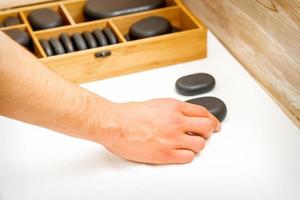 mano de masajista toma negro masaje piedras desde el mesa en spa salón. foto