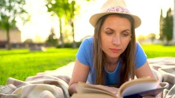 menina dentro óculos lendo livro deitado baixa em uma cobertor dentro a parque às pôr do sol video