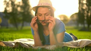 Girl in glasses reading book lying down on a blanket in the park at sunset video