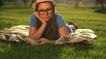 niña en lentes leyendo libro acostado abajo en un cobija en el parque a puesta de sol video