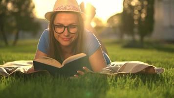 fille dans des lunettes en train de lire livre mensonge vers le bas sur une couverture dans le parc à le coucher du soleil video