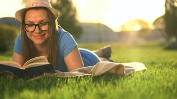 niña en lentes leyendo libro acostado abajo en un cobija en el parque a puesta de sol video
