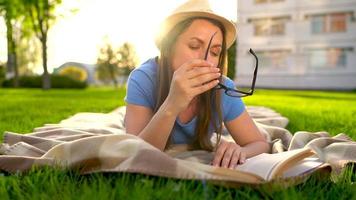 menina dentro óculos lendo livro deitado baixa em uma cobertor dentro a parque às pôr do sol video