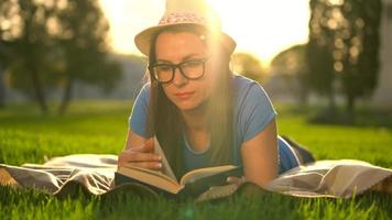 niña en lentes leyendo libro acostado abajo en un cobija en el parque a puesta de sol video