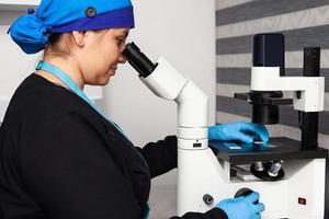 Female scientist looking at slides with patient samples using an inverted microscope in the laboratory. photo