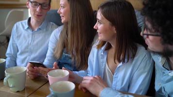 Young friends sit in a cafe, drink coffee and have fun communicating. Slow motion video