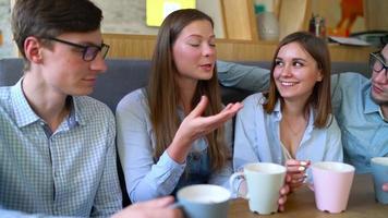 Young friends sit in a cafe, drink coffee and have fun communicating. Slow motion video