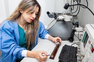 joven hembra científico cargando un cuadrícula con un muestra en el muestra poseedor de un transmisión electrón microscopio foto