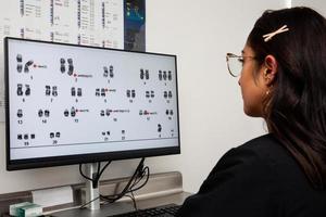 Computer screen showing a human karyotype. Young female scientis photo