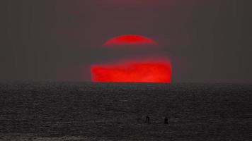 escénico paisaje rojo Dom a puesta de sol por el mar. siluetas de personas en un tabla de surf o cenar tablero en contra el fondo de el Dom video