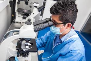 joven masculino científico mirando a diapositivas debajo el microscopio foto