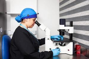 Female scientist looking at slides with patient samples using an inverted microscope in the laboratory. photo